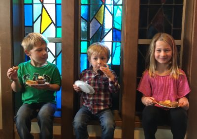 Children sit in the window sill of the stained glass windows and enjoy snacks from coffee hour after church.